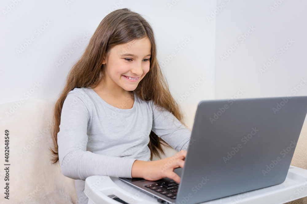 Portrait of attractive cute happy smiling girl 6-7 old sitting using laptop indoor white background distance learning Portrait of attractive cute happy smiling girl 6-7 old sitting using laptop indoor white background distance learning
