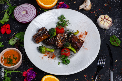 Grilled pork ribs in honey glaze with tomatoes and broccoli on a dark background