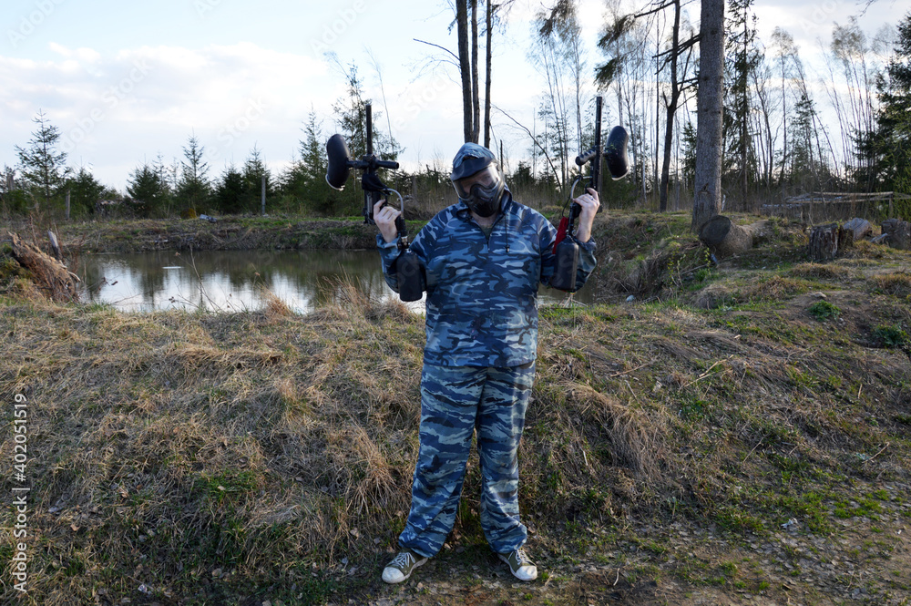 Man in camouflage clothing aiming a paintball guns. Boy in a protective suit and mask Man in camouflage clothing aiming a paintball guns. Boy in a protective suit and mask