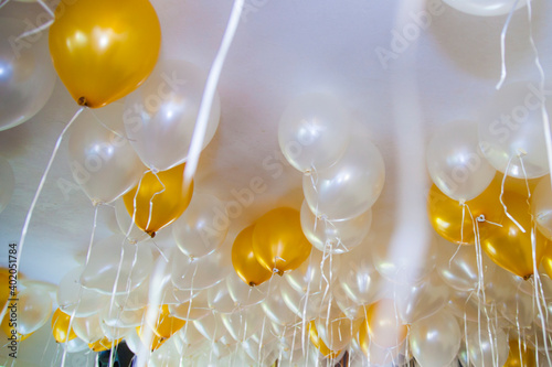 A group of rising helium balloons in white and gold color on a ceiling of an apartment as decorative elements at a party