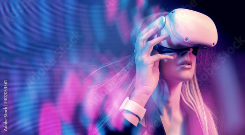 young woman with blond hair in a vr helmet looks around with surprise and delight
