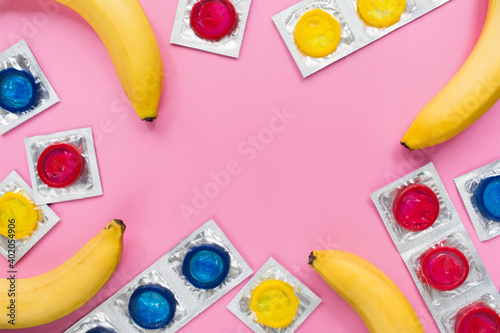 Composition with colorful condoms and bananas on pink background. Safe sex and contraceptive concept. Flat lay, top view, copy space. photo