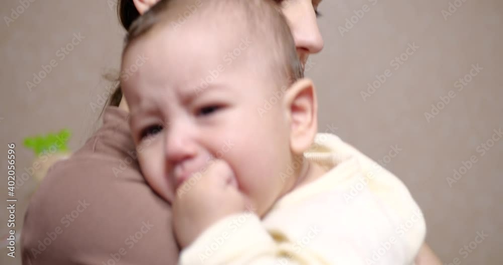 mom comforts and hugs a crying newborn baby in her arms. baby in mom's arms looking at the camera. Motherhood concept mom comforts and hugs a crying newborn baby in her arms. baby in mom's arms looking at the camera. Motherhood concept