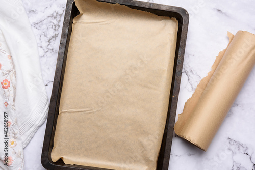 empty rectangular metal baking sheet and roll of brown parchment paper on white background