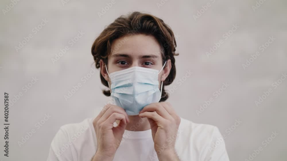Young attractive man puts on a medical face mask as protection against the Coronavirus. He smiles and looks into the camera. Covid-19 measurements. Young attractive man puts on a medical face mask as protection against the Coronavirus. He smiles and looks into the camera. Covid-19 measurements.