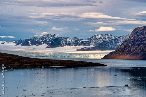 Beautiful bay view in Svalbard with glaciers in the distance and sky reflecting on the water while a zodiac glides by in the foreground.