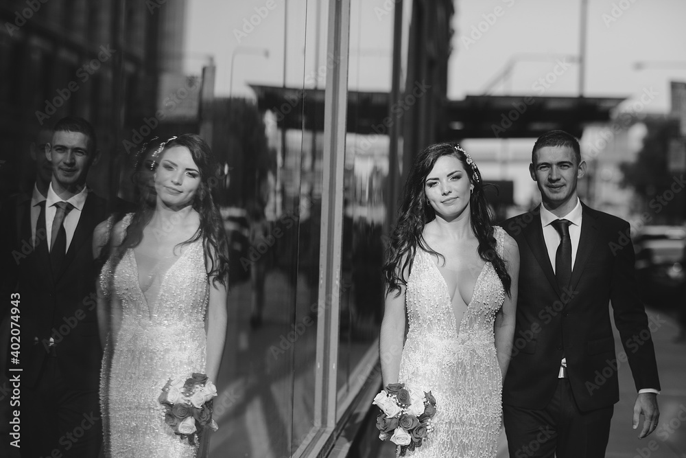 Naklejka premium Elegant wedding couple walking in a summer city. Man in a blue suit. Woman in a white elegant dress with bouquet of roses