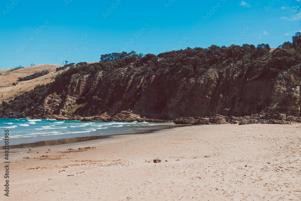 pristine wild landscape at Clifton Beach in Tasmania, Australia with wavy blue ocean and golden sand next to a rugged coastline