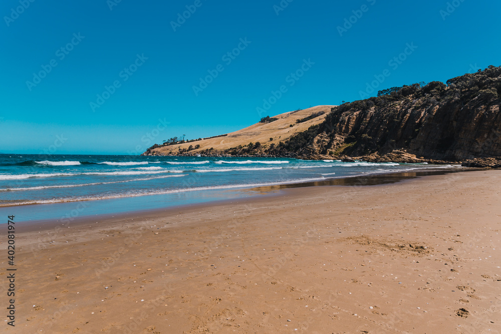 pristine wild landscape at Clifton Beach in Tasmania, Australia with wavy blue ocean and golden sand next to a rugged coastline pristine wild landscape at Clifton Beach in Tasmania, Australia with wavy blue ocean and golden sand next to a rugged coastline