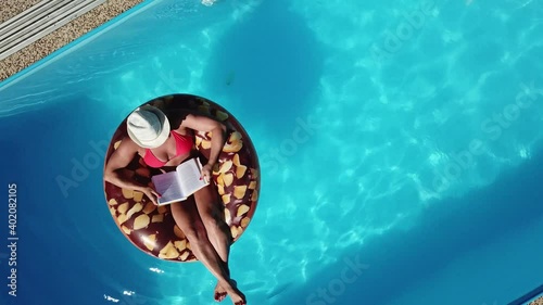 Young woman enjoying summer fun by the hotel pool. The girl relaxes with a book by the water. Wellness resort. Aerial view.