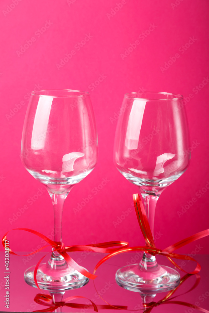 Two champagne glasses with red ribbons on a pink background. Two champagne glasses with red ribbons on a pink background.