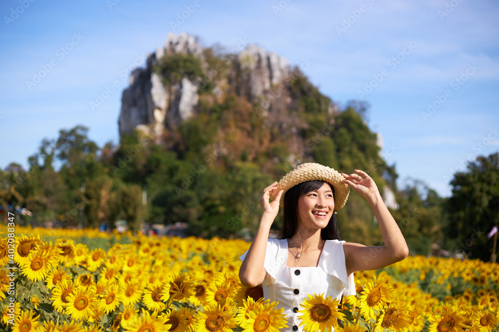 A young Asian attractive woman in a straw hat stands in a sunflower field.