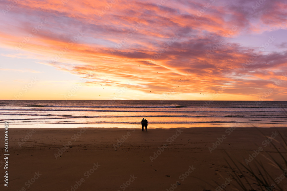 Couple embracing each other by the bach with stunning sunrise