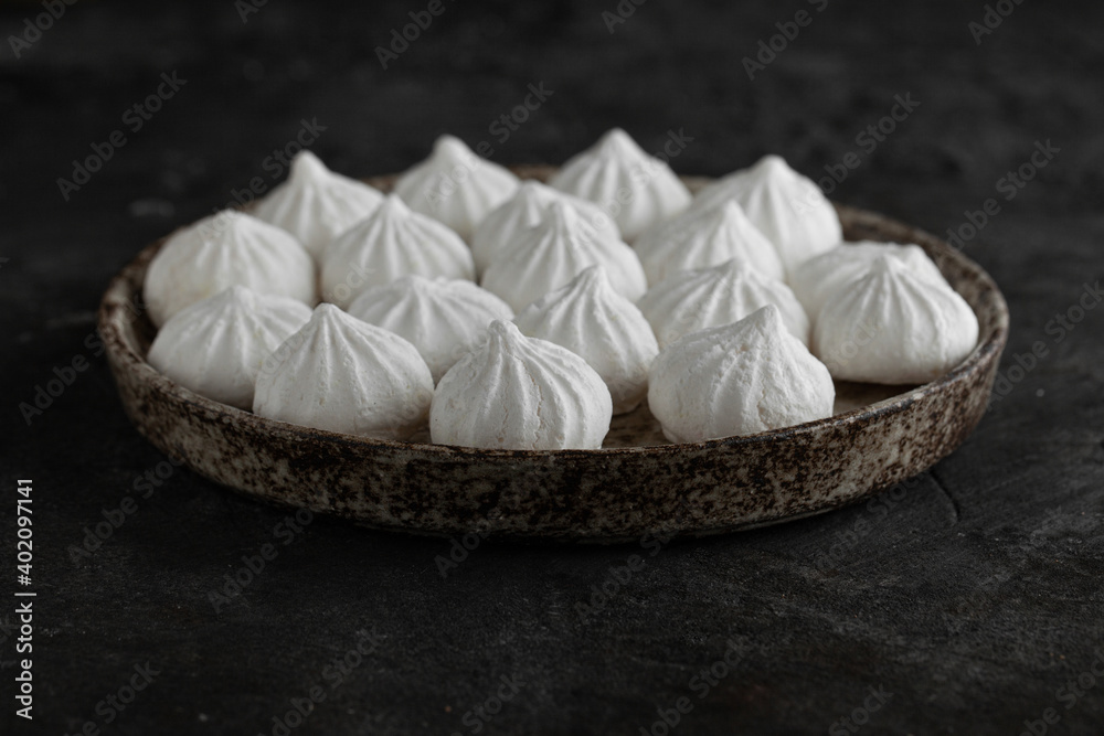 White sweet meringue in ceramic round bowl and plate on concrete background.
