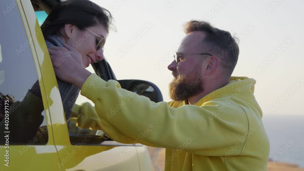 Happy bearded man stands near car, while his his girlfriend sits in car and smiles at him Happy bearded man stands near car, while his his girlfriend sits in car and smiles at him