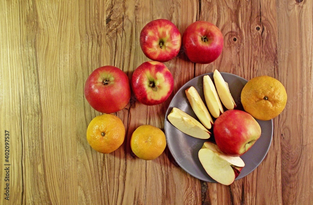 red apples and tangerines on an oak table, some of which lie on a platter red apples and tangerines on an oak table, some of which lie on a platter