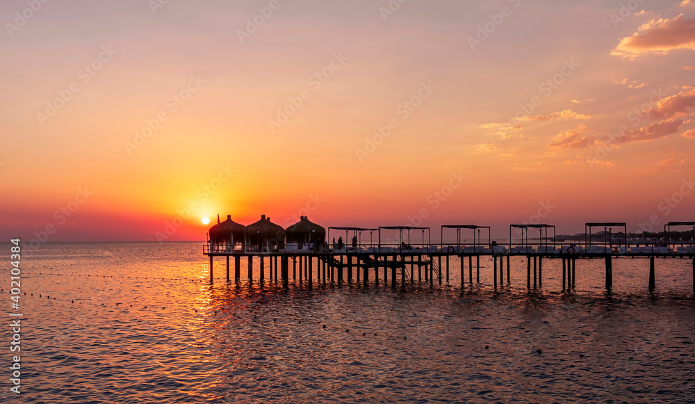amazing picturesque view at a pier in sea with calm water and beautiful sunset on a background. Scenic costal view on shoreline with hotel in tourist season