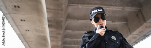 portrait of policewoman in sunglasses talking on radio set on urban street, banner.