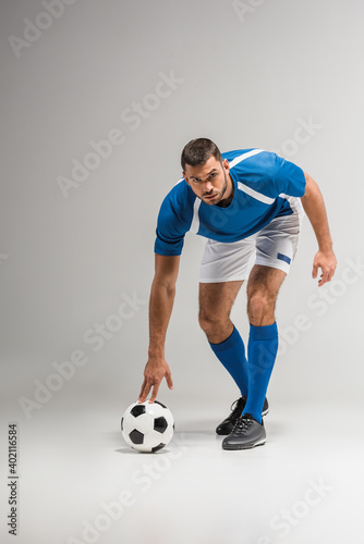 Confident sportsman looking at camera near football on grey background