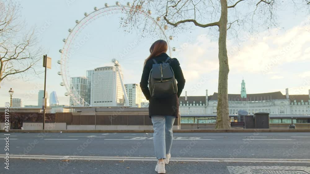 A girl tourist with backpack walking on London empty streets in lockdown. A female in a coat during winter walking in front of most famous London landmarks in slow-motion in 4K.