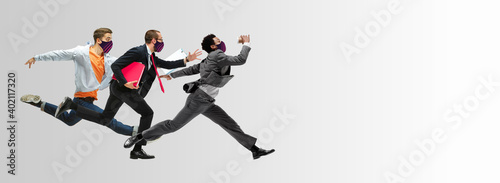 Happy office workers in face masks jumping and dancing in casual clothes or suit isolated on studio background. Business, start-up, prevention of COVID, motion and action concept. Creative collage.