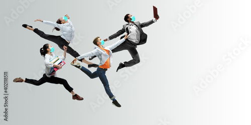 Happy office workers in face masks jumping and dancing in casual clothes or suit isolated on studio background. Business, start-up, prevention of COVID, motion and action concept. Creative collage.