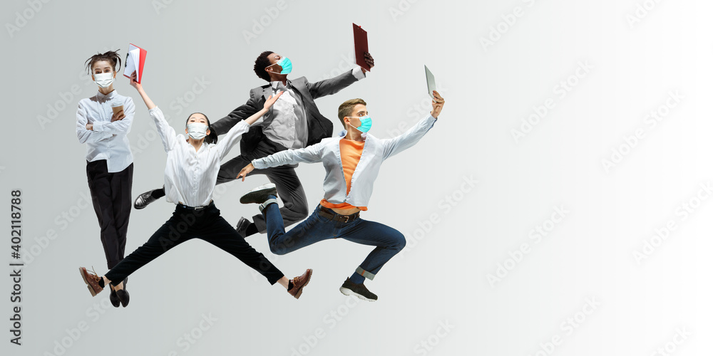 Happy office workers in face masks jumping and dancing in casual clothes or suit isolated on studio background. Business, start-up, prevention of COVID, motion and action concept. Creative collage.