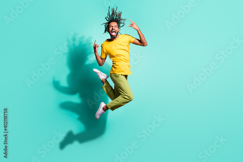 Full size photo of young happy smiling crazy excited afro man jumping show rock n roll sign isolated on turquoise color background