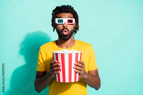 Photo of young shocked amazed surprised african man in 3-D glasses watch movie eat pop corn isolated on teal color background