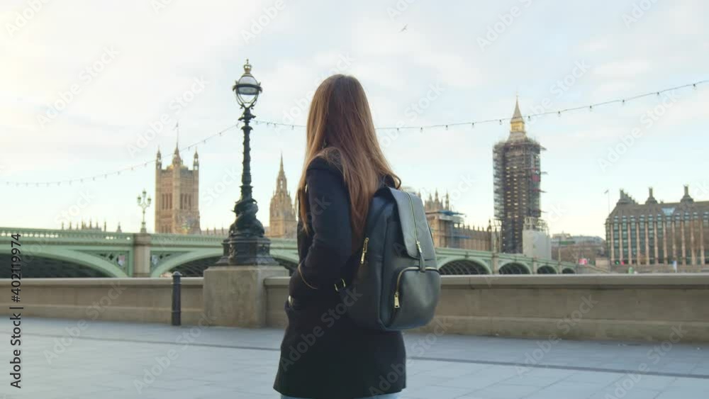 A girl tourist with backpack walking on London empty streets in lockdown. A female in a coat during winter walking in front of most famous London landmarks in slow-motion in 4K.