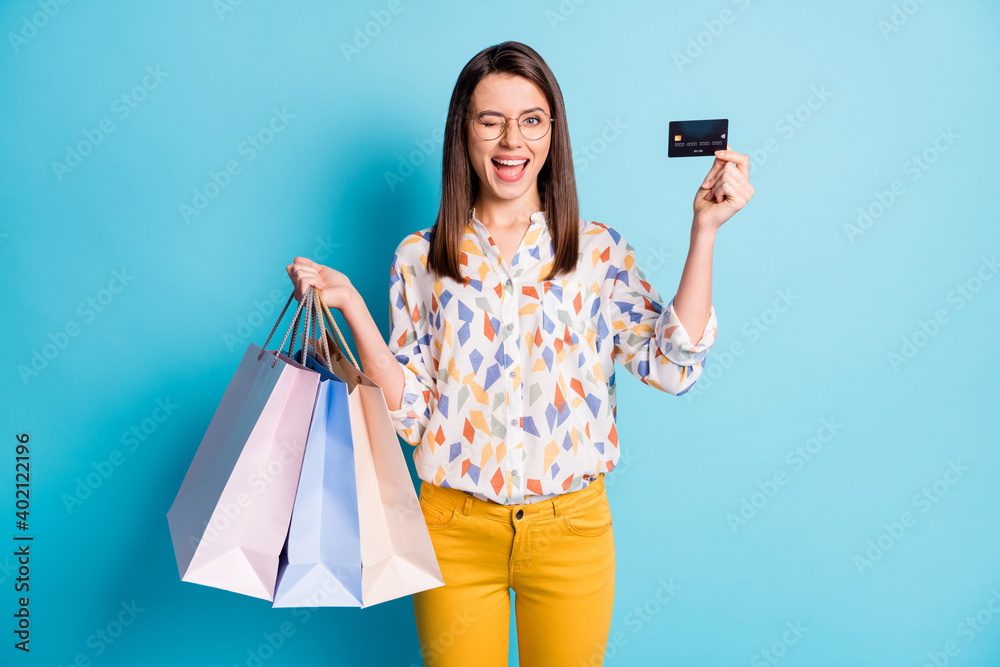 Photo of lady hold credit card blink eye many bags wear glasses geometry print shirt yellow trousers isolated blue color background Photo of lady hold credit card blink eye many bags wear glasses geometry print shirt yellow trousers isolated blue color background