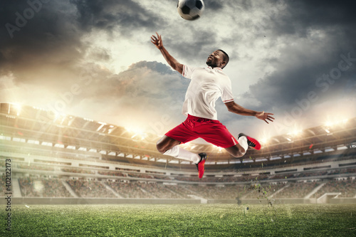 Jumping up. Young male soccer or football player kicking ball during match at the stadium in flashlights, spotlights. Concept of professional sport, motion, movement. 3D render. Flyer for ad.