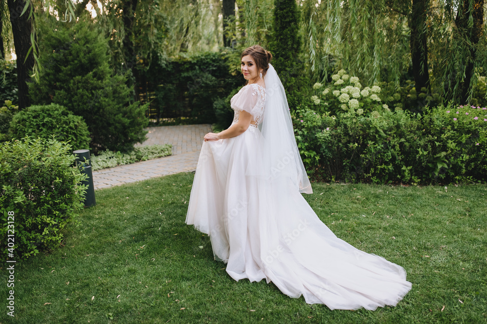 A beautiful curly-haired bride in a long lace white dress is walking on the grass in the meadow, against the backdrop of green plants and trees. Wedding portrait of newlyweds in love. A beautiful curly-haired bride in a long lace white dress is walking on the grass in the meadow, against the backdrop of green plants and trees. Wedding portrait of newlyweds in love.