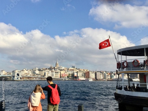 Canvas Print Young couple on beach looking at the Golden Horn in Istanbul with ferry and distance view of Galata bridge and tower
