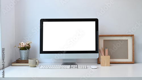 Front view of minimal workspace with mock up computer pot plant, frame, coffee cup on white desk. Blank screen for graphics display montage.