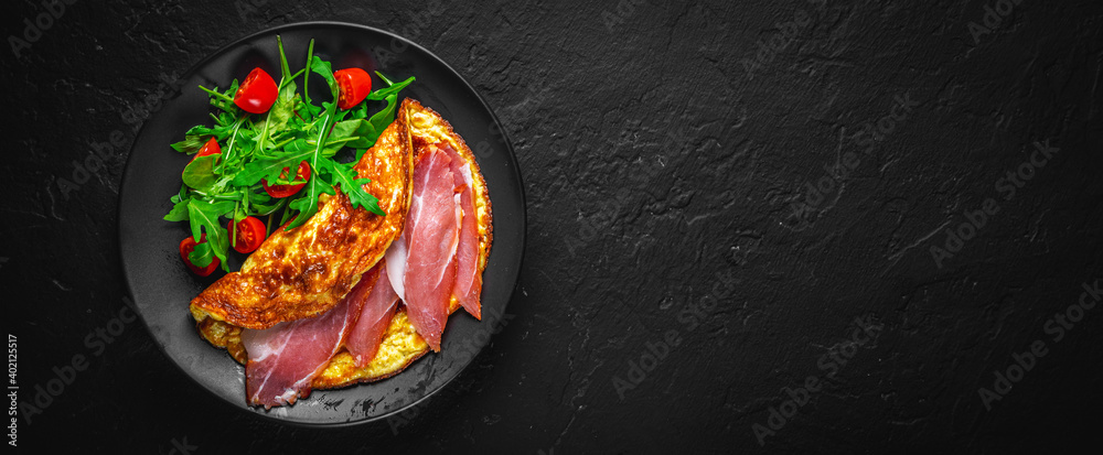 omelette with prosciutto and salad on black plate on Dark grey black slate background
