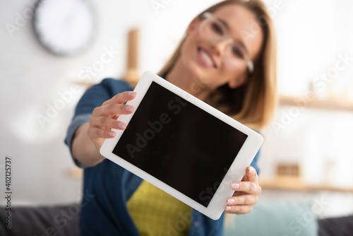  blonde woman looking at camera while showing digital tablet on blurred background