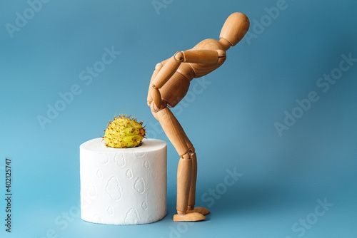 Wooden figure sit on a roll of toilet paper. Concept of the problem with hemorrhoids.