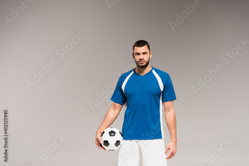 Sportsman in sportswear holding football and looking at camera isolated on grey