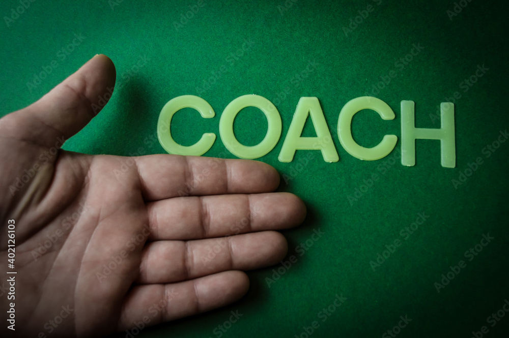 Human hand showing the word Coach written with plastic letters on green paper background, concept Human hand showing the word Coach written with plastic letters on green paper background, concept
