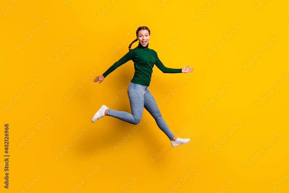 Full length body size photo smiling woman jumping high laughing wearing jeans isolated on vivid yellow color background