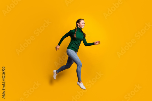 Full length body size side profile photo laughing girl jumping high running fast isolated on vibrant yellow color background © deagreez
