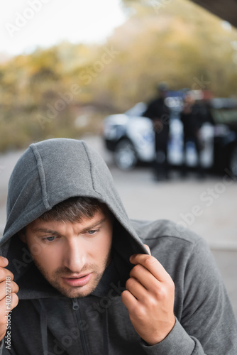 scared hooded offender hiding with blurred police officers on background outdoors.