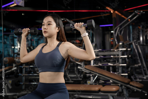 young Athletic woman with muscular body exercising Crossfit. Asian Woman in sportswear doing a workout with the dumbbell at the gym © Adulwit