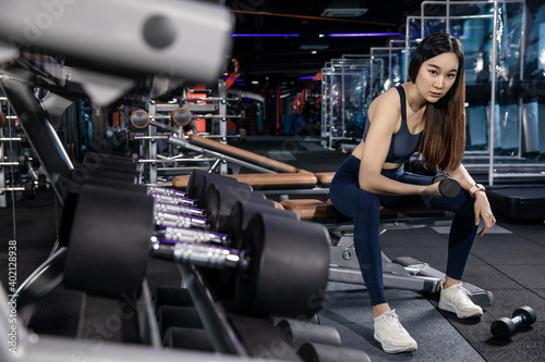 young Athletic woman with muscular body exercising Crossfit. Asian Woman in sportswear doing a workout with the dumbbell at the gym
