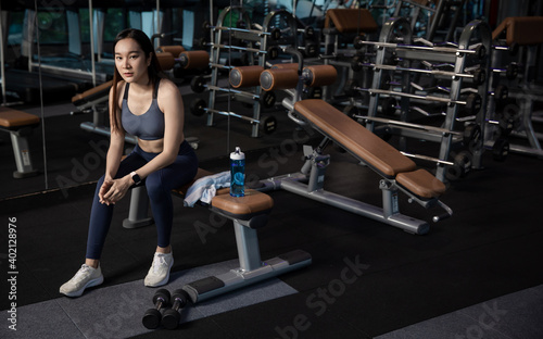 Young woman sitting on a chair at gym after her workout. Female athlete taking rest after exercising at gym.