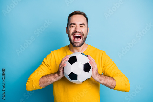 Photo portrait of amazed cheerful man keeping football ball shouting isolated on vibrant blue color background © deagreez