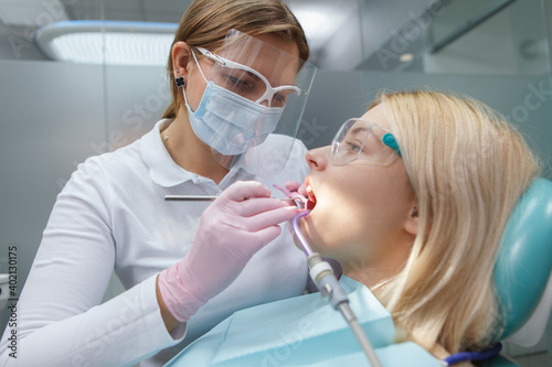 Female dentist wearing protective face mask  treating teeth of female patient