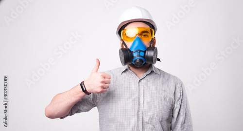 Portrait of man using respirator and wearing helmet and showing thumb up gesture.