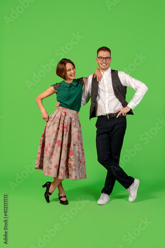 Disco. Old-school fashioned young woman dancing isolated on green studio background. Artist fashion, motion and action concept, youth culture, fashion returning. Young stylish man and woman.